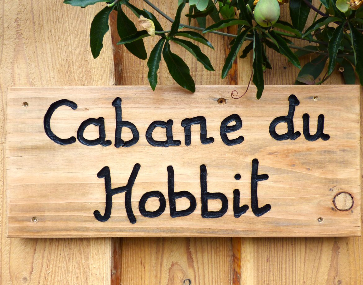 Cabane du Hobbit en Auvergne, avec une enseigne en bois rustique et verdure environnante.