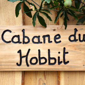 Cabane du Hobbit en Auvergne, avec une enseigne en bois rustique et verdure environnante.