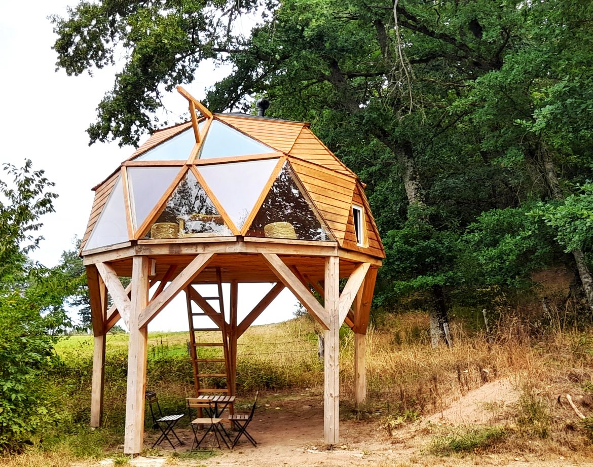Cabane géodésique en bois, perchée sur pilotis, entourée de verdure en Auvergne.