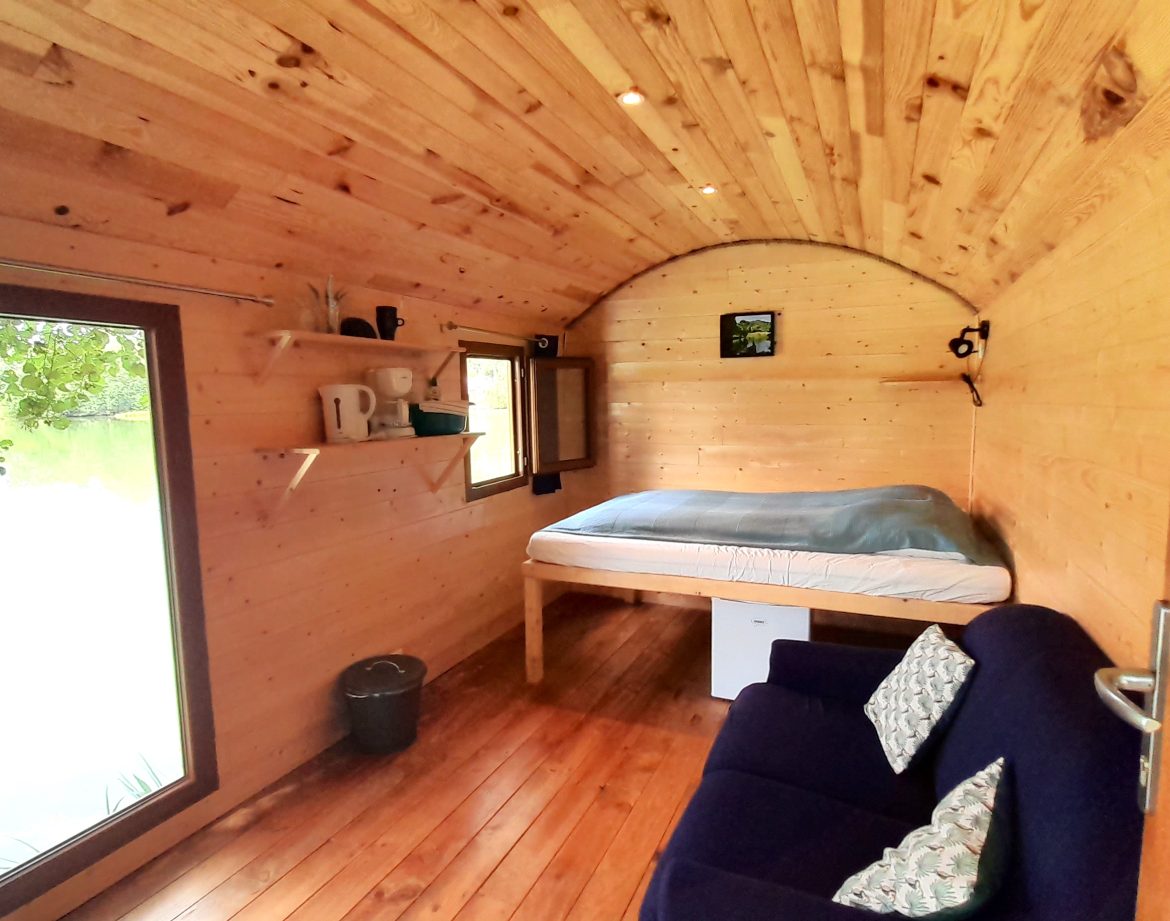 Cabane en bois au bord de leau, intérieur chaleureux avec lit et canapé confortable.