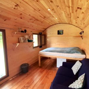 Cabane en bois au bord de leau, intérieur chaleureux avec lit et canapé confortable.