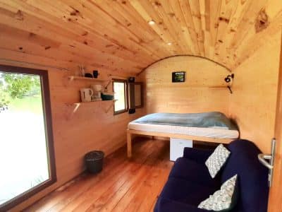 Cabane en bois au bord de leau, intérieur chaleureux avec lit et canapé confortable.