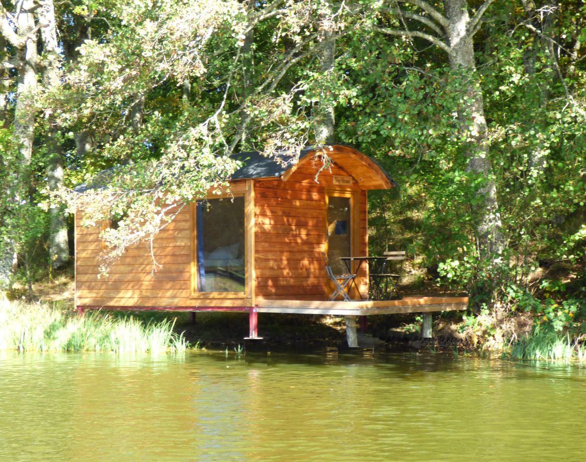 Cabane en bois sur pilotis au bord dun lac, entourée darbres verdoyants.