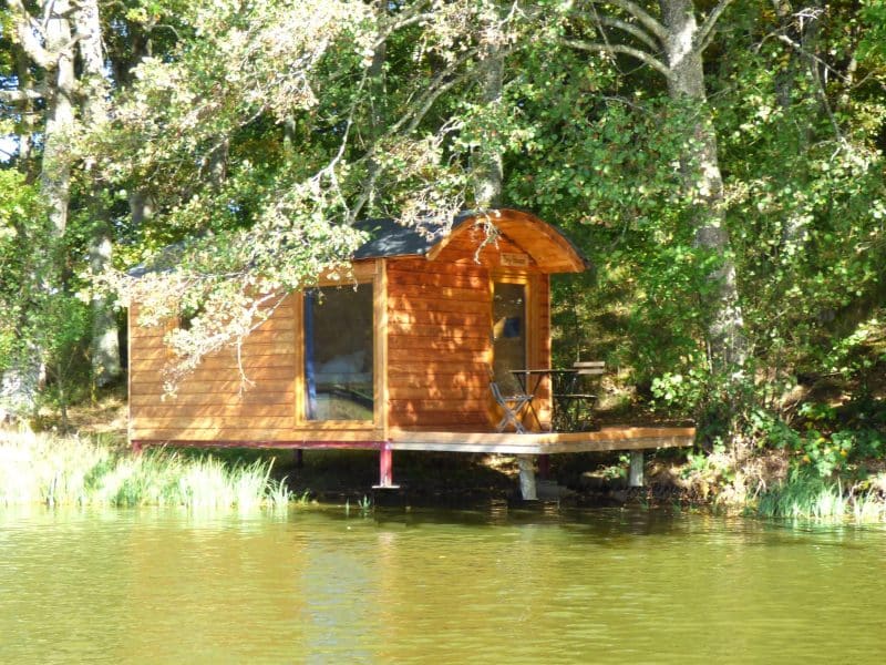 Cabane en bois sur pilotis au bord dun lac, entourée darbres verdoyants.
