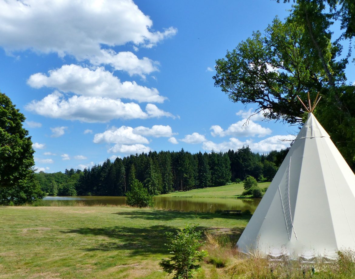 Tipi au bord dun lac en Auvergne, entouré de verdure et ciel bleu.