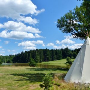 Tipi au bord dun lac en Auvergne, entouré de verdure et ciel bleu.
