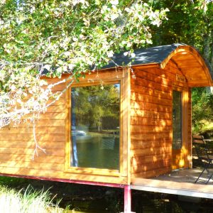 Cabane sur pilotis en bois, entourée de verdure, au bord dun étang paisible.