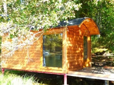 Cabane sur pilotis en bois, entourée de verdure, au bord dun étang paisible.