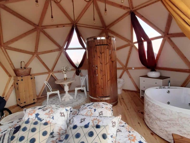 Dôme géodésique avec lit douillet, baignoire en marbre et décor chaleureux.