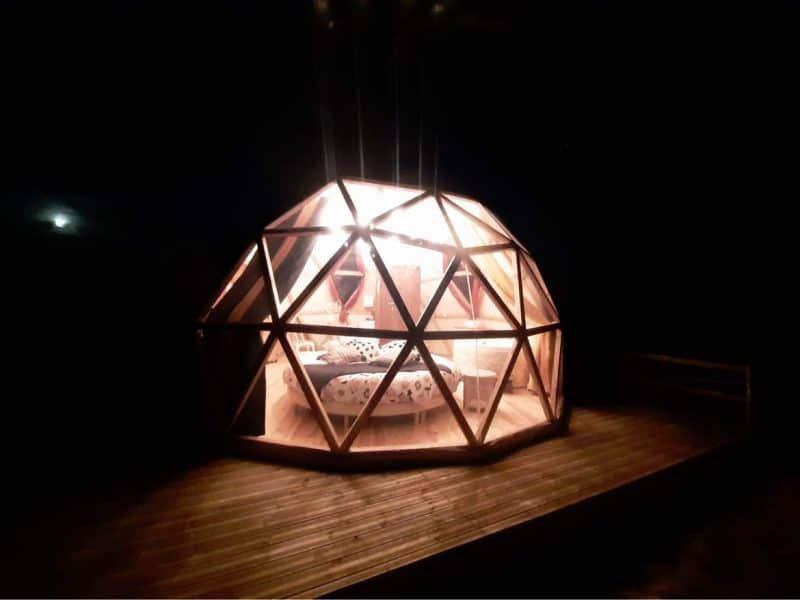 Dôme en bois lumineux, offrant une vue nocturne sur la nature environnante.