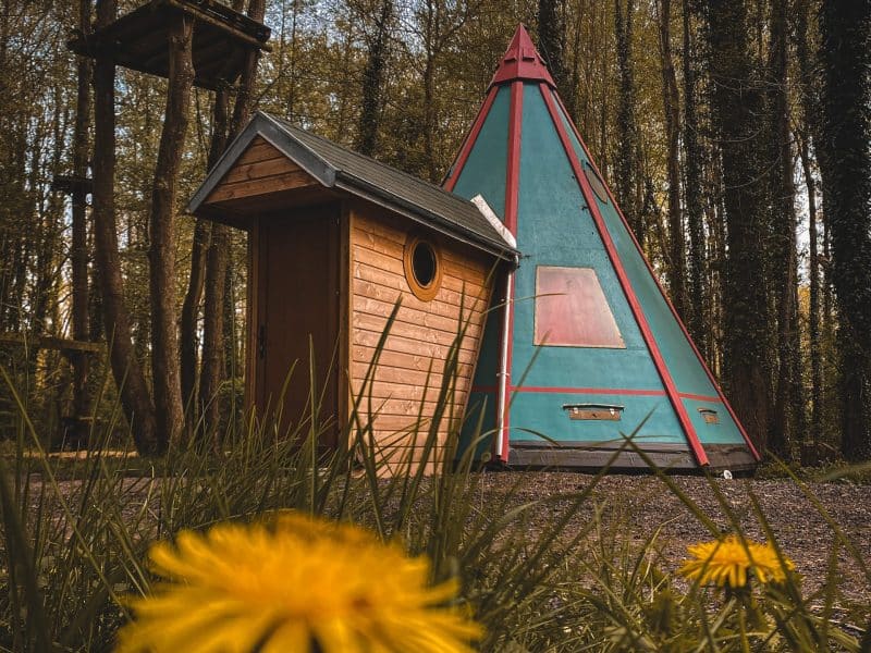 Tente tipi colorée et cabane en bois, nichées au cœur dune forêt verdoyante.