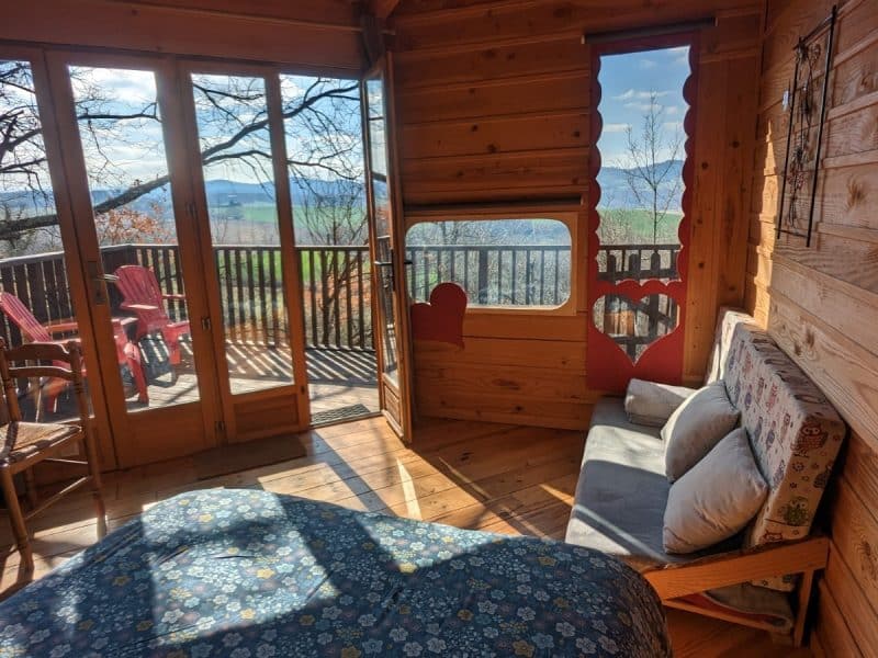 Cabane en bois avec vue panoramique, lit confortable et balcon ensoleillé.
