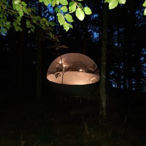 Hébergement insolite en bulle transparente, illuminée sous les arbres en Auvergne.