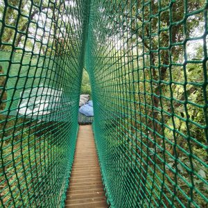 Hébergement insolite : cabane dans les arbres avec passerelle en filet vert.