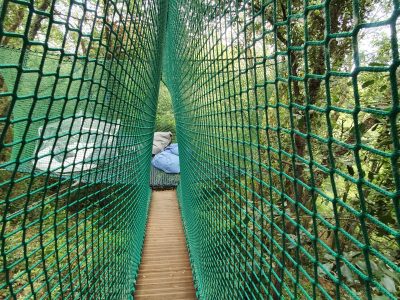 Hébergement insolite : cabane dans les arbres avec passerelle en filet vert.