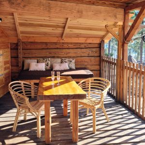 Cabane en bois avec terrasse ensoleillée et vue sur la nature environnante.