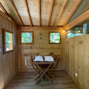 Cabane en bois chaleureuse avec table et fenêtres offrant une vue sur la nature.