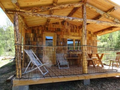 Cabane en bois avec terrasse ensoleillée et chaises confortables en Auvergne-Rhône-Alpes.