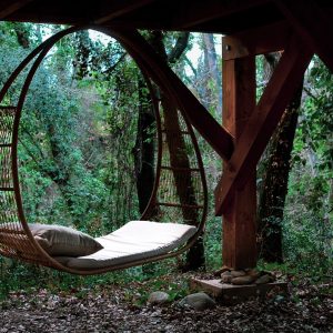 Hébergement insolite : hamac suspendu en osier, entouré de verdure luxuriante.