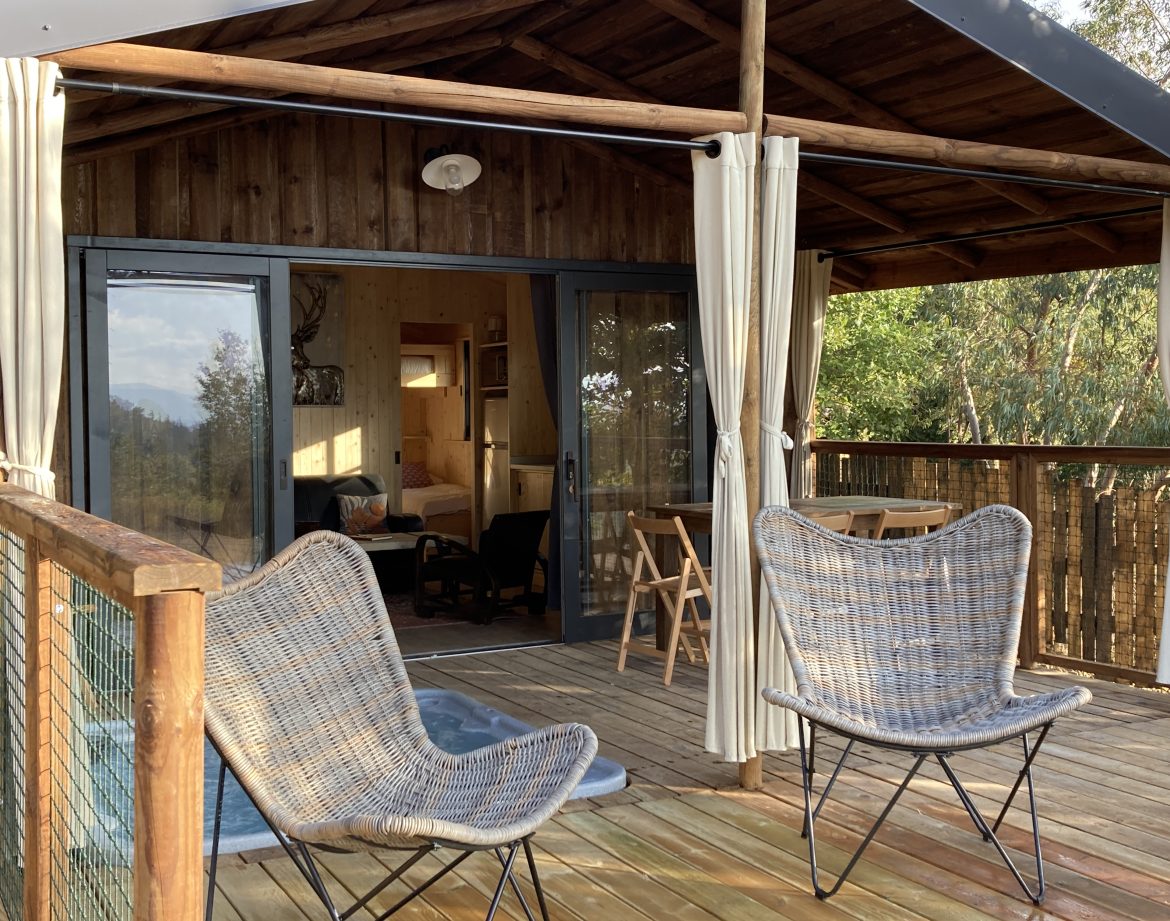 Cabane perchée en bois avec terrasse, chaises confortables et vue sur la nature.