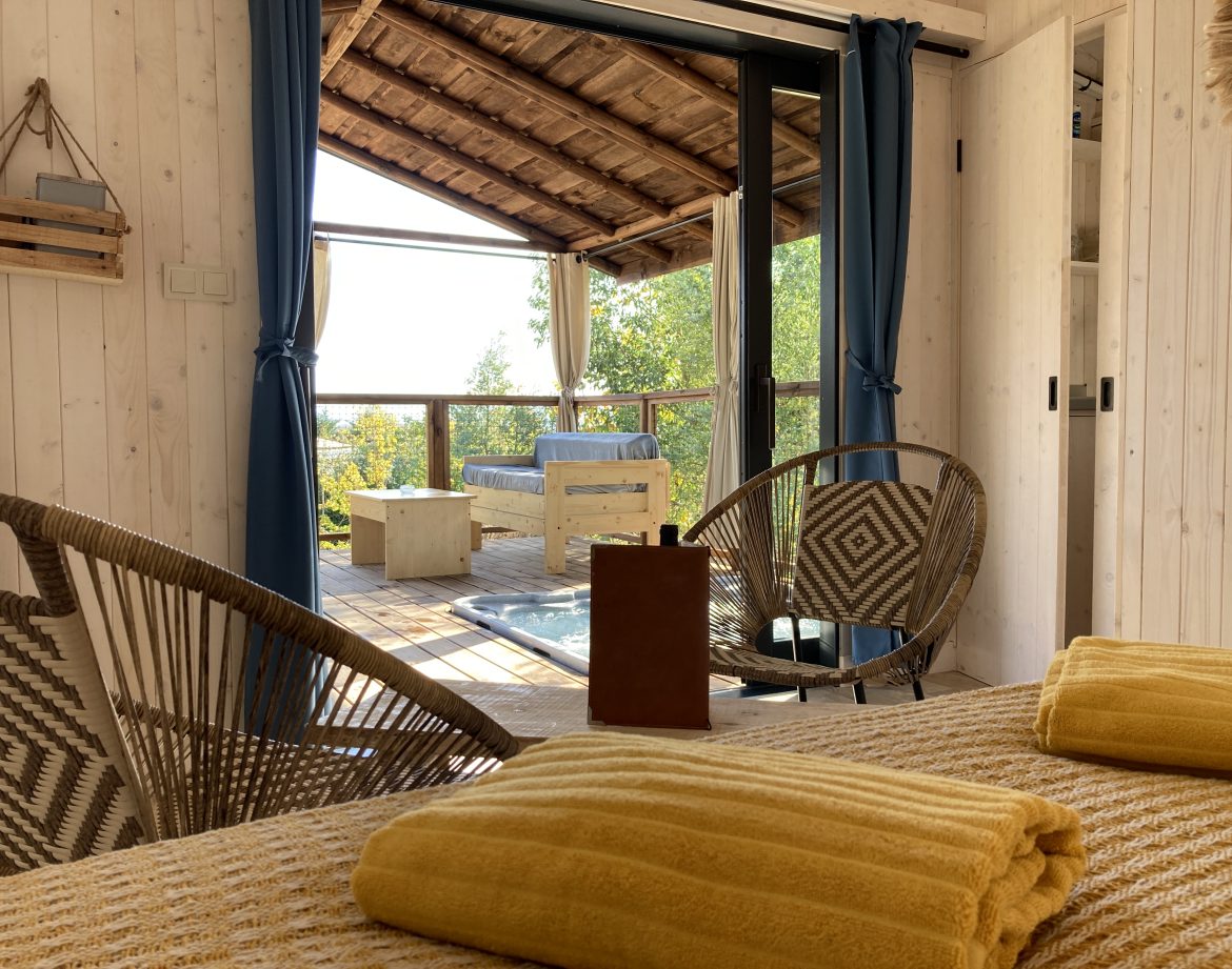 Cabane en bois avec vue, décorée de coussins jaunes et fauteuils en rotin.