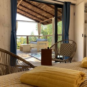 Cabane en bois avec vue, décorée de coussins jaunes et fauteuils en rotin.