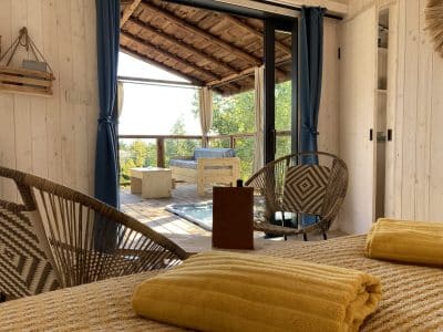 Cabane en bois avec vue, décorée de coussins jaunes et fauteuils en rotin.