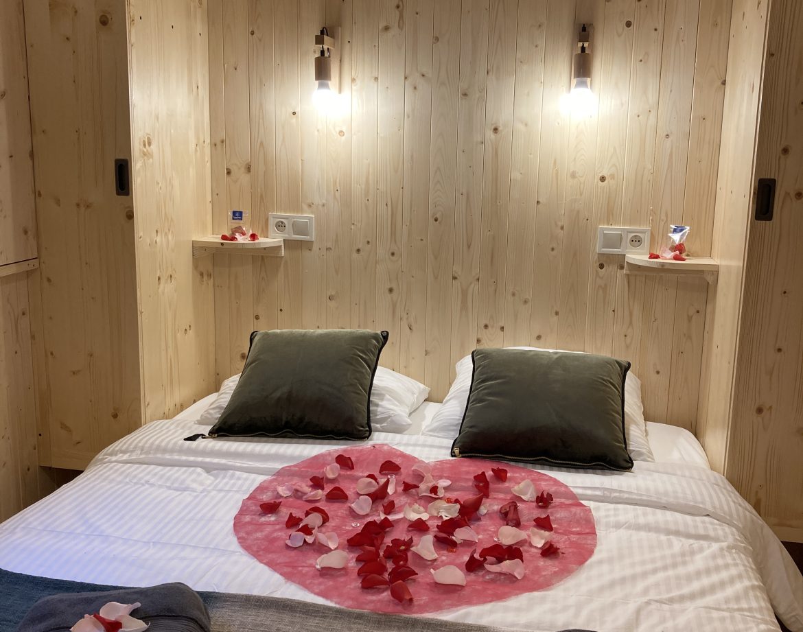 Chalet en bois romantique avec pétales de fleurs sur le lit. Idéal pour un séjour cocooning.