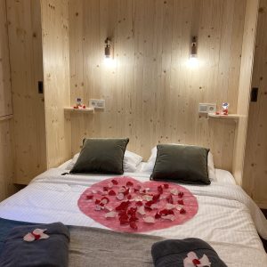 Chalet en bois romantique avec pétales de fleurs sur le lit. Idéal pour un séjour cocooning.