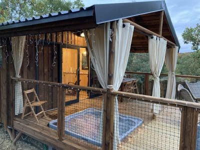 Cabane en bois avec jacuzzi, entourée de verdure et décorée de guirlandes lumineuses.