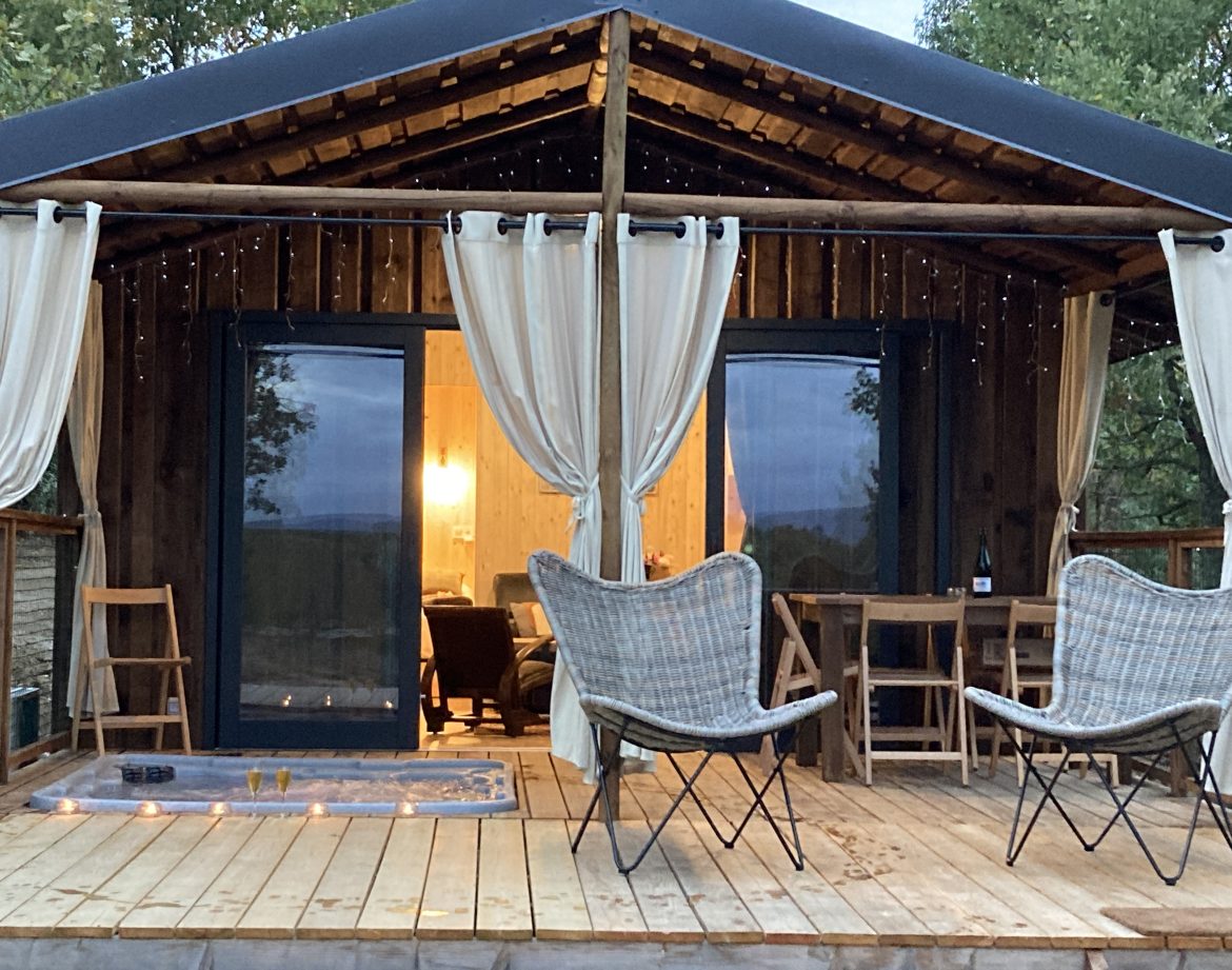 Cabane en bois avec terrasse, éclairage doux et chaises confortables.