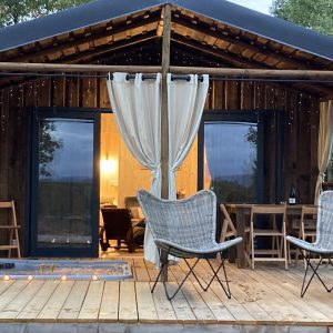 Cabane en bois avec terrasse, éclairage doux et chaises confortables.