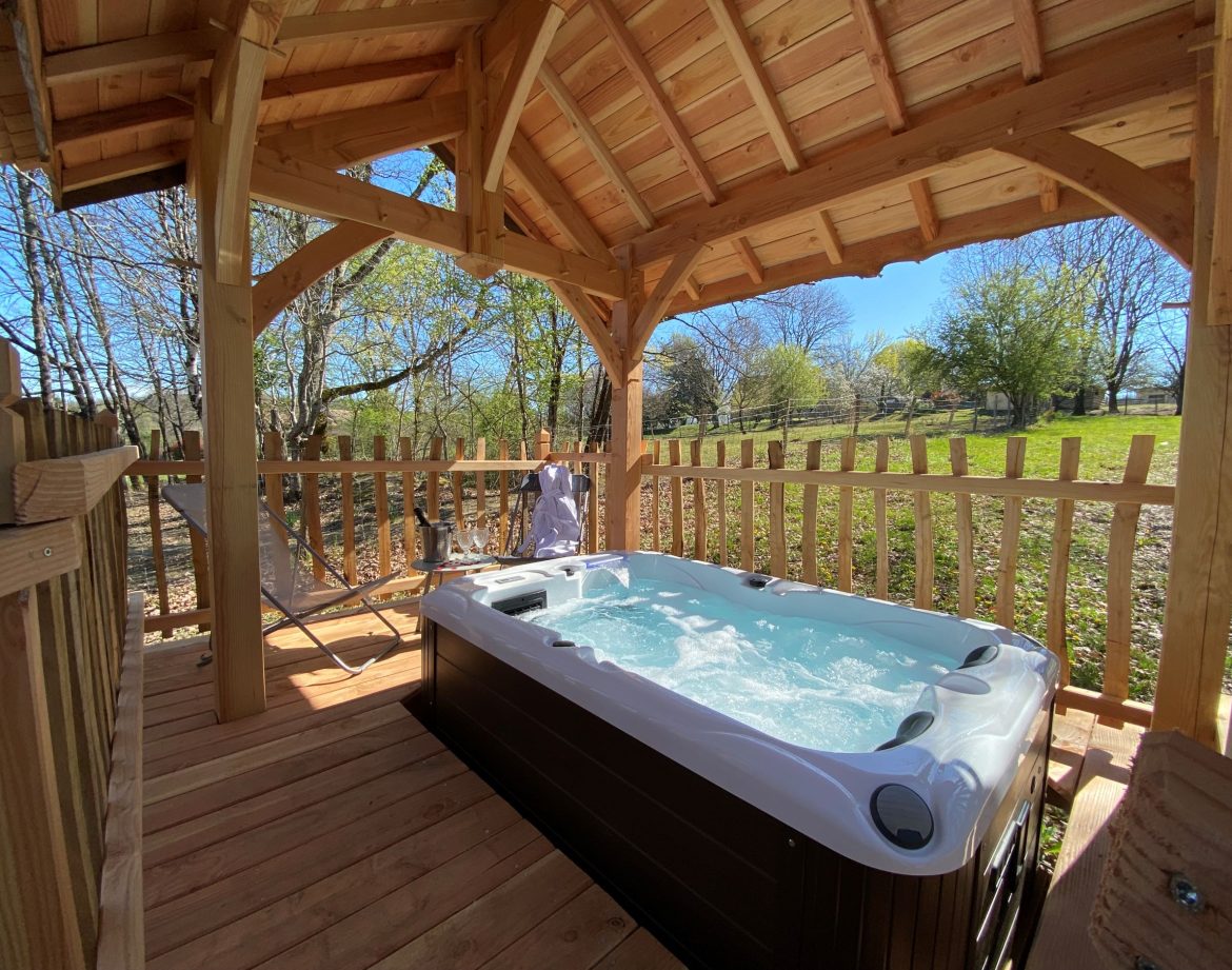 Hébergement insolite en Aquitaine avec jacuzzi sous un abri en bois, entouré de verdure.