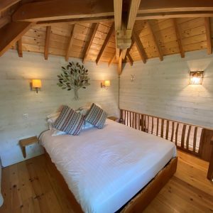 Chalet en bois avec un lit douillet et un plafond en poutres apparentes.