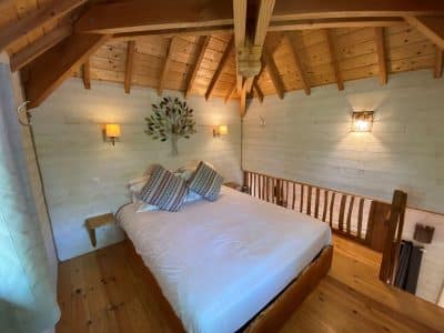 Chalet en bois avec un lit douillet et un plafond en poutres apparentes.