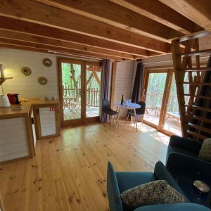 Cabane en bois dans les arbres, avec un intérieur lumineux et un coin salon cosy.