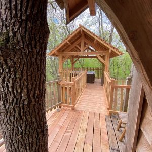 Cabane perchée en bois avec terrasse, entourée darbres verdoyants en Aquitaine.