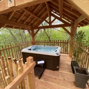 Hébergement insolite en Aquitaine avec jacuzzi sous un abri en bois, entouré de verdure.