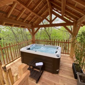 Hébergement insolite en Aquitaine : cabane en bois avec jacuzzi entouré de verdure.