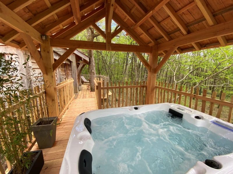 Hébergement insolite en Aquitaine avec jacuzzi sous un abri en bois, entouré de verdure.