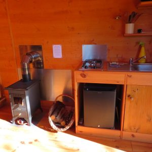 Intérieur chaleureux dun chalet en bois en Bretagne, avec poêle à bois et cuisine équipée.