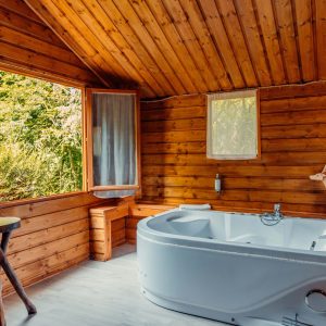 Cabane en bois avec baignoire, grandes fenêtres offrant une vue sur la nature.