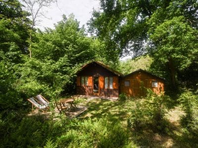 Cabane en bois nichée dans la verdure, avec chaises longues et terrasse accueillante.
