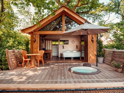 Cabane perchée en bois avec terrasse, vue sur la nature et jacuzzi extérieur.
