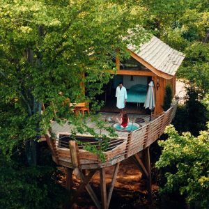 Cabane perchée dans les arbres, avec terrasse et vue sur la nature environnante.