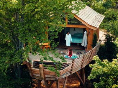 Cabane perchée dans les arbres, avec terrasse et vue sur la nature environnante.