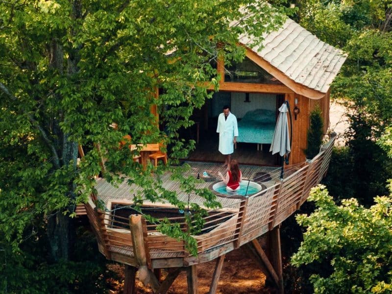 Cabane perchée dans les arbres, avec terrasse et vue sur la nature environnante.