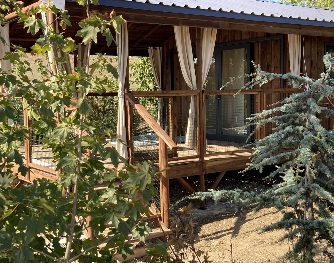 Cabane en bois avec terrasse, entourée de verdure, dans le Languedoc-Roussillon.