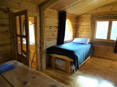 Chalet en bois chaleureux avec lit simple et grandes fenêtres lumineuses.