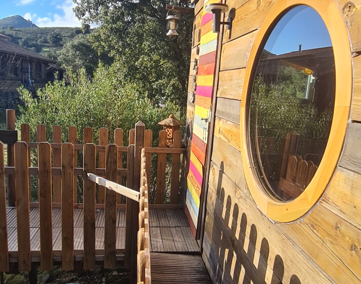 Cabane en bois colorée en Corse, avec une terrasse en bois et une vue verdoyante.